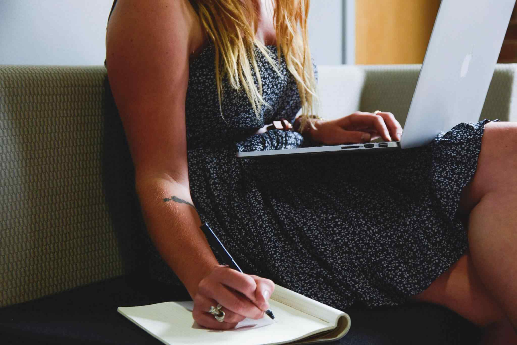 Woman writing while using a laptop.