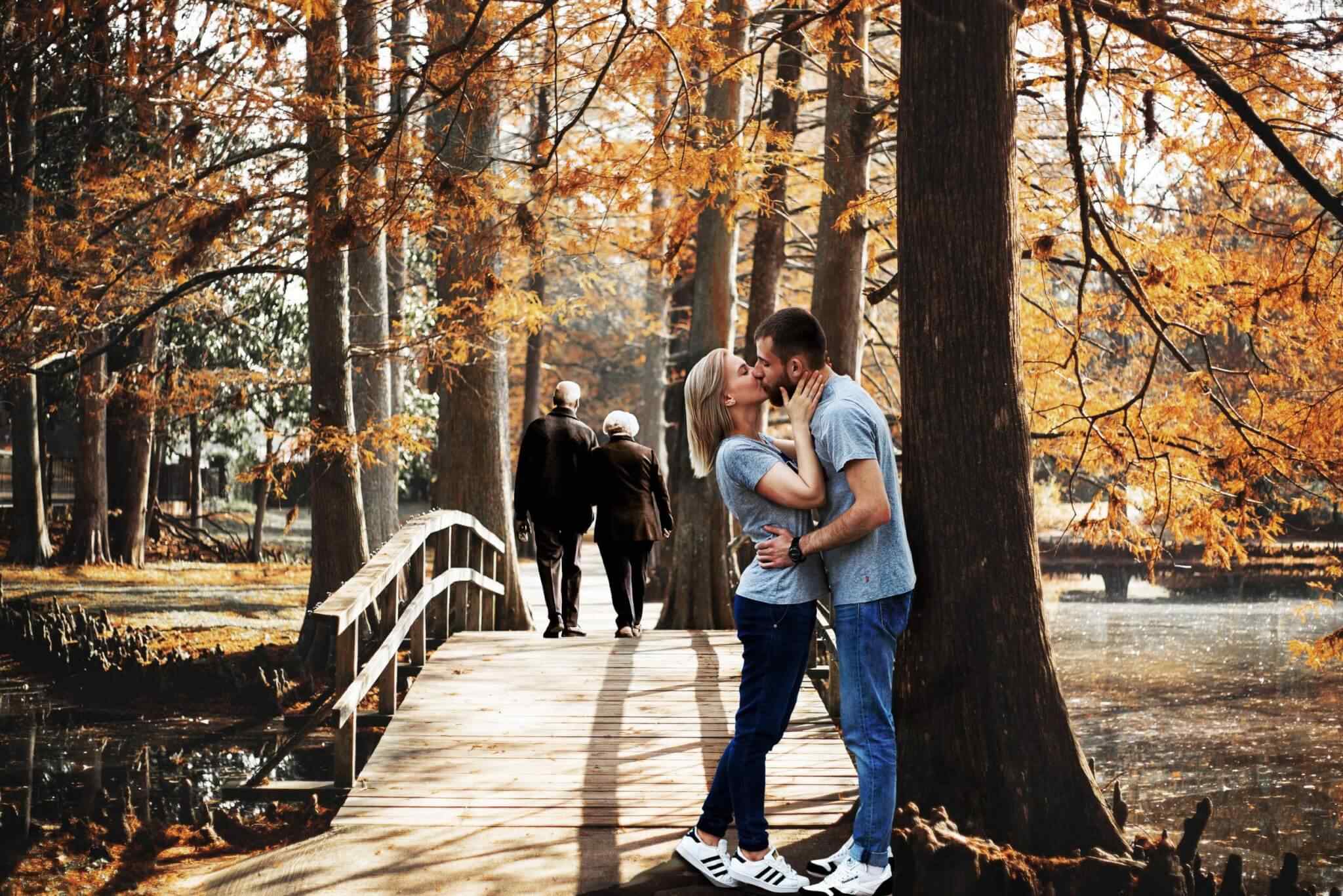 Couple kissing on autumn forest bridge.