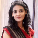 Woman wearing glasses and red outfit smiling.