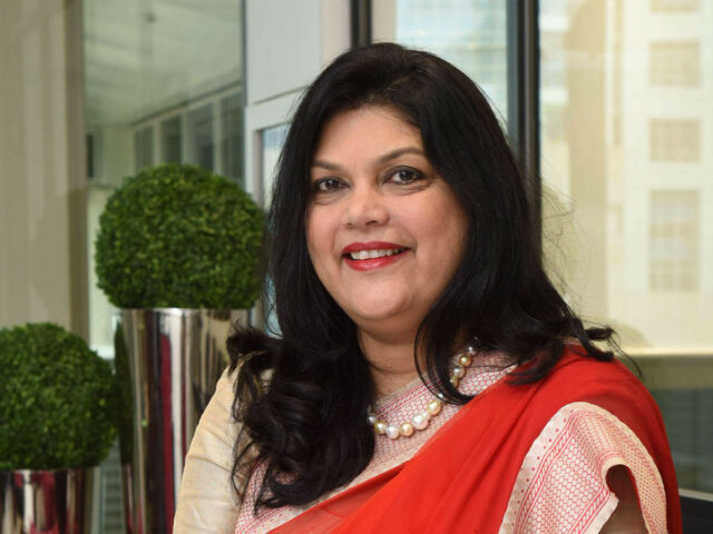 Smiling woman in red saree indoors.